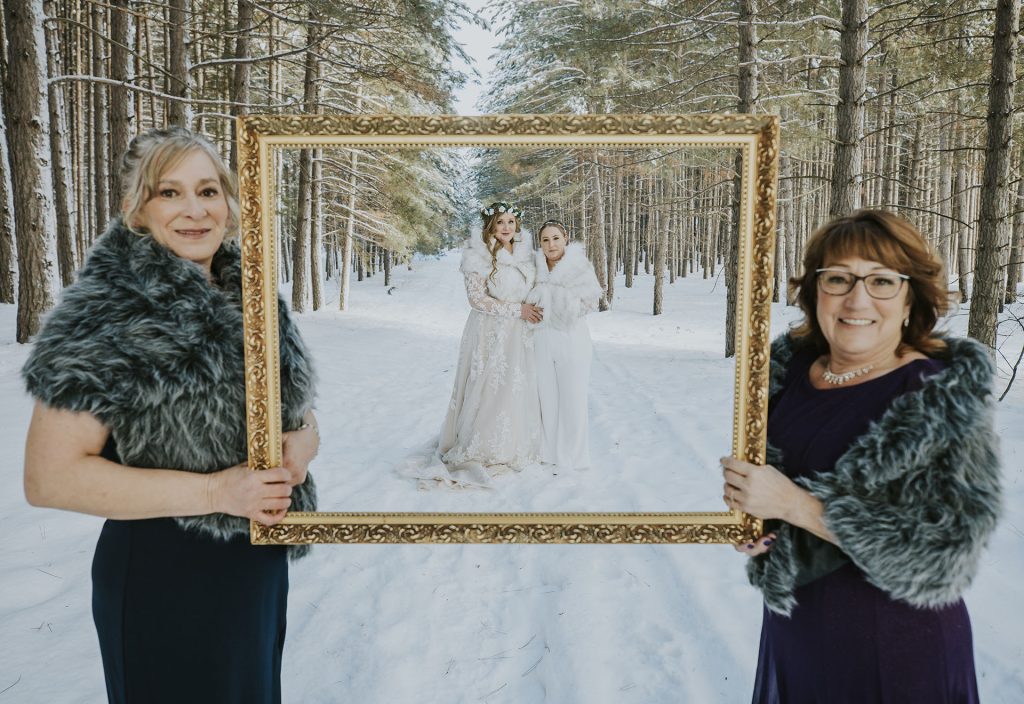 Moms holding an empty frame with the brides behind it for a photo in the snow in Sudbury, Ontario